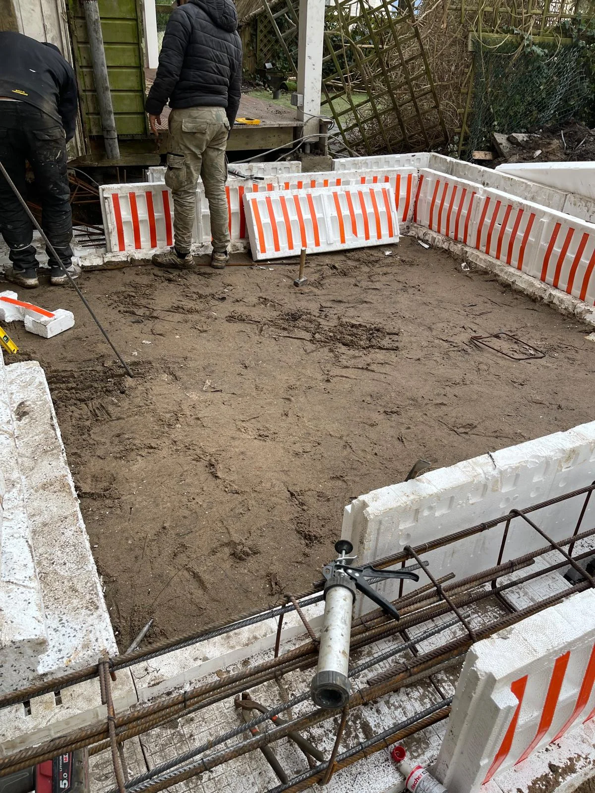 De wapeningskorf voor de funderingsbalken tussen verloren EPS-bekisting, met doorgevoerde rioleringsbuis.