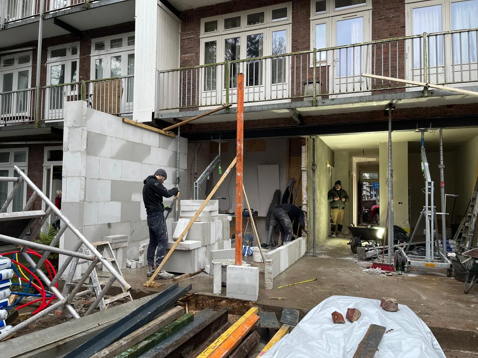 Een metselaar zet een kalkzandsteenblok op dunbedmortel; drie vakmannen werken in ritme.