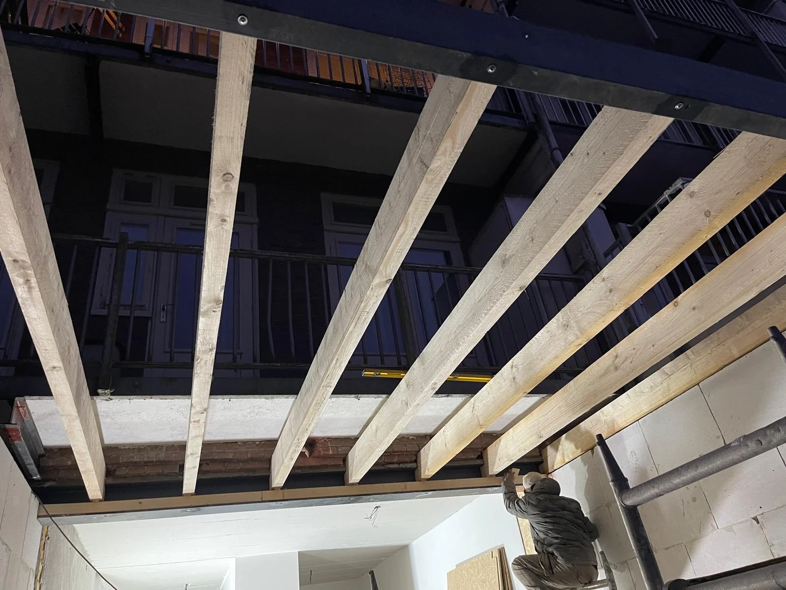 Houten dakbalken opgelegd op de zwarte HEB-ligger, verankerd in de kalkzandsteen-zijwand.