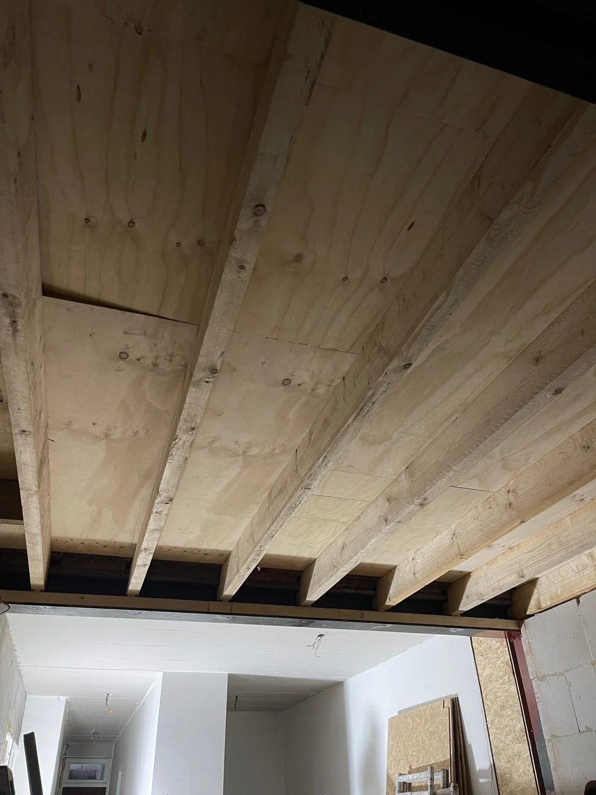 Plafondaanzicht van de nieuwe aanbouw: ritmische houten balken met multiplex-schroting.
