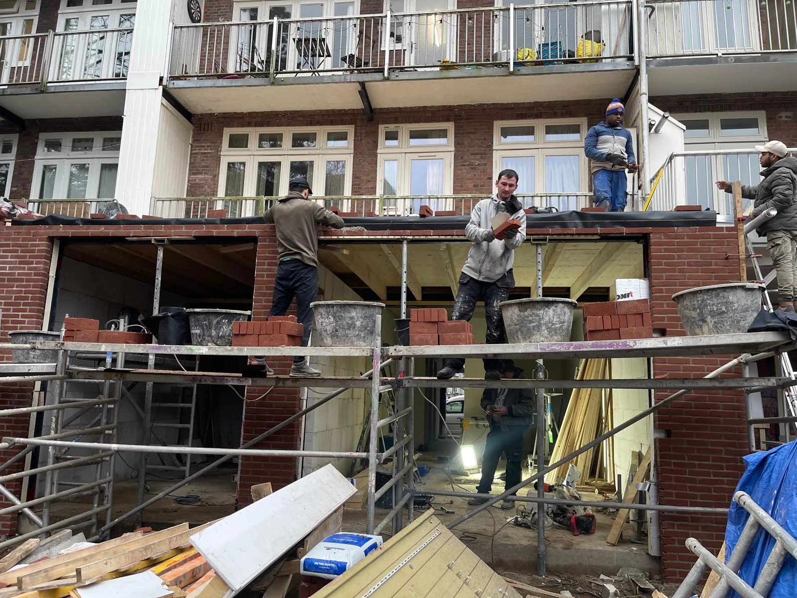 Vijf vakmannen op een professionele steiger werken aan de laatste lagen baksteen.