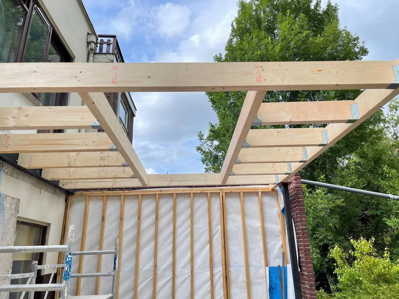 De complete balklaag van het dak, gezien vanaf de tuinzijde tegen de bestaande woning.