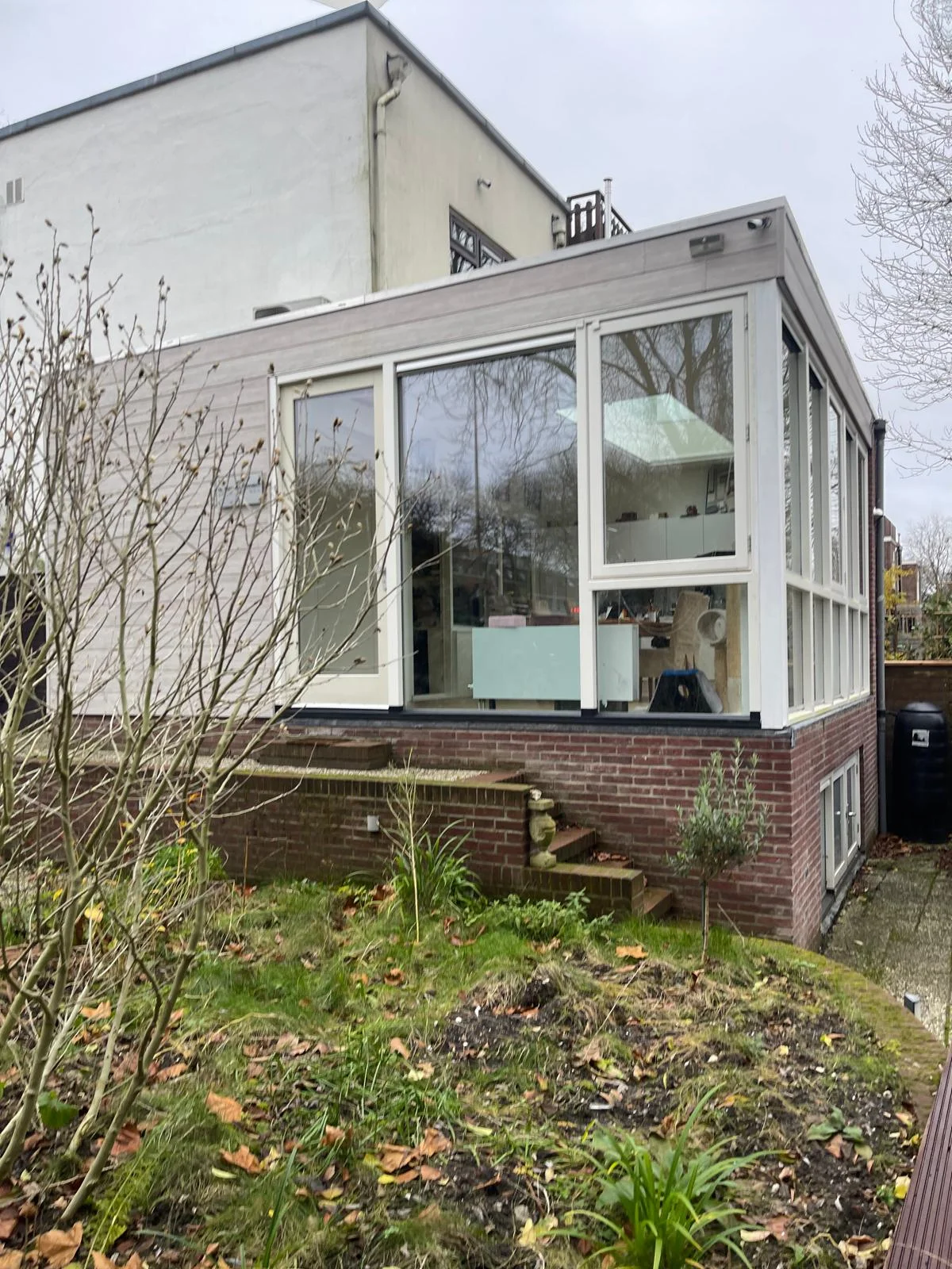 De opgeleverde aanbouw vanaf het lager gelegen tuinniveau: brede glaspui, podium en tuintrap in rood metselwerk, berging onder de woonkamer.
