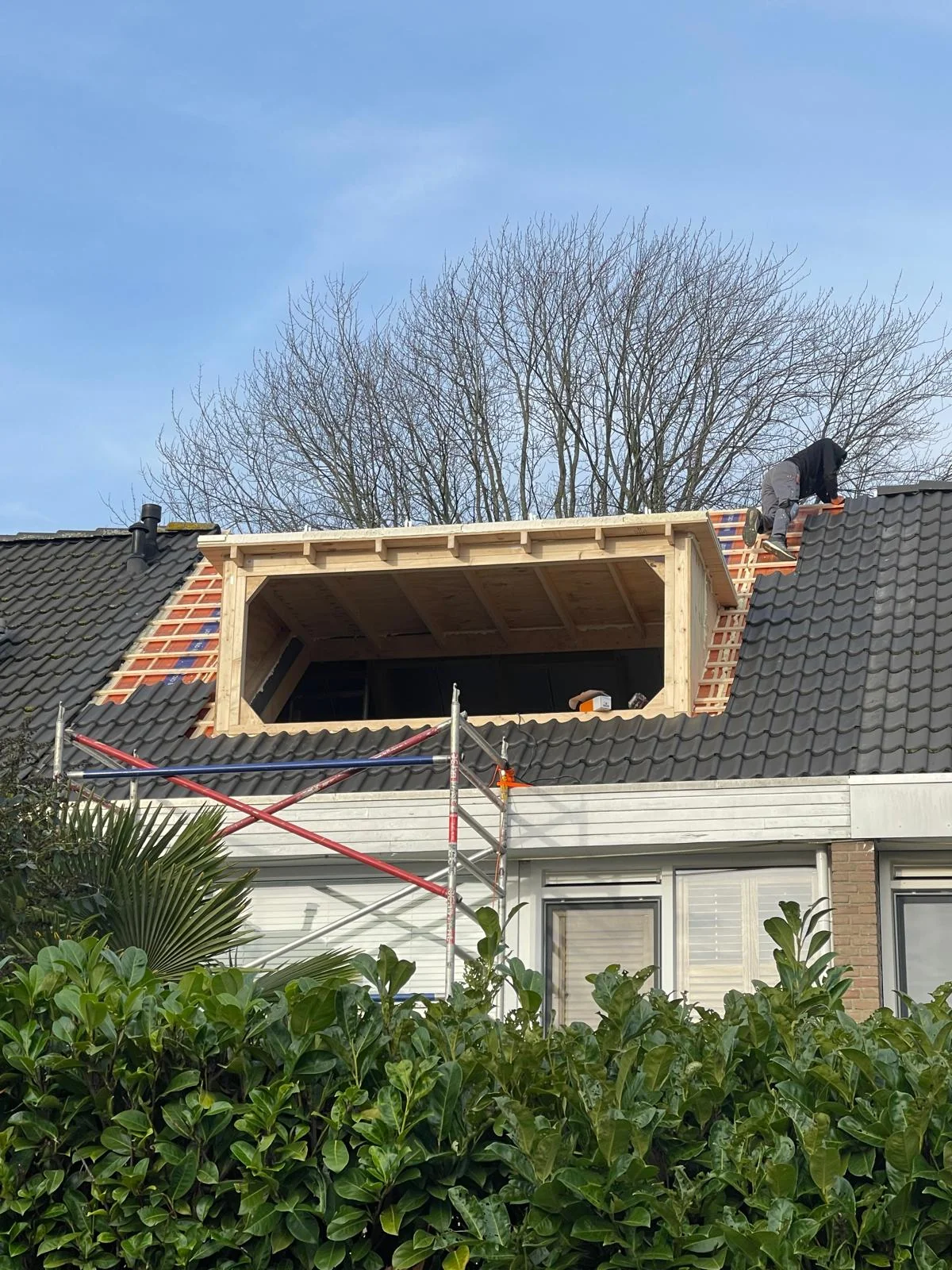 Het houten skelet van de nieuwe dakkapel staat, met een vakman die de verbindingen controleert.