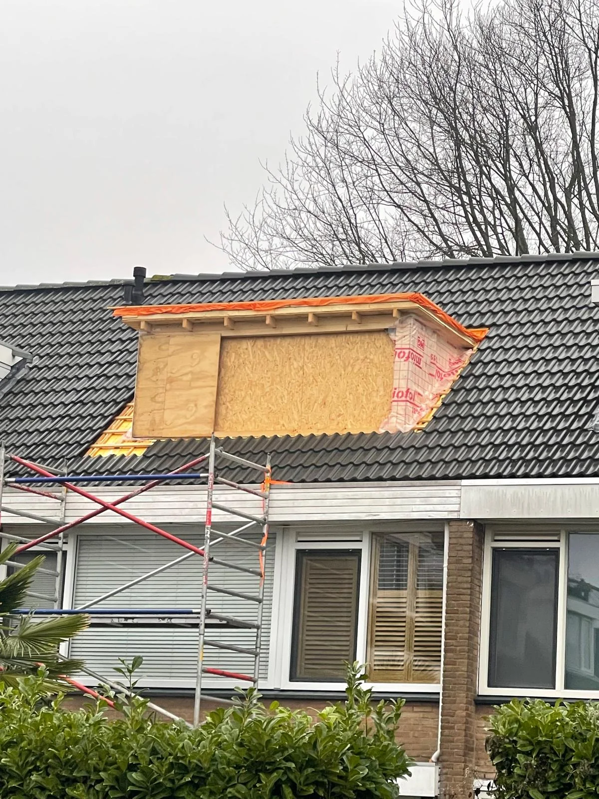 De dakkapel dichtgemaakt met multiplex onderplaat, eerste antraciet-zwarte pannen rondom.