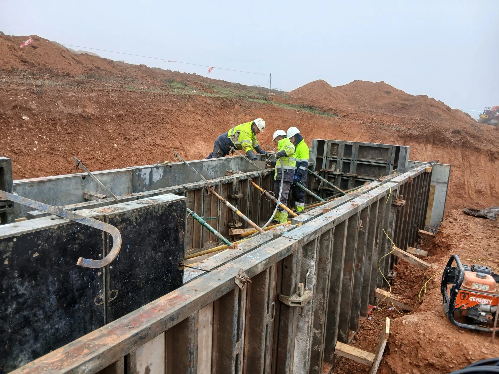 Twee vakmannen werken aan de bovenste lagen van een wapeningskorf, vlak voor de stort, met donker bekistingssysteem rondom.